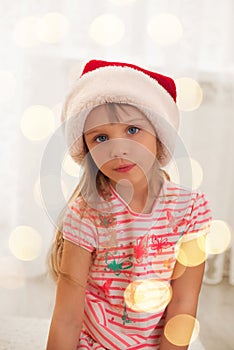 Cute little girl in Santa's hat enjoying at home. Holiday lights photo