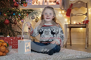 Cute little girl in a Scandinavian sweater at the Christmas tree.