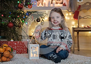 Cute little girl in a Scandinavian sweater at the Christmas tree.