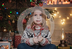 Cute little girl in a Scandinavian sweater at the Christmas tree.