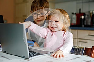 Cute little girl and school kid boy and looking at laptop, Two children, brother and sister using pc or notebook, e