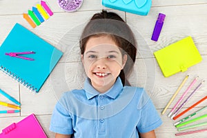 Cute little girl with school stationery on wooden background
