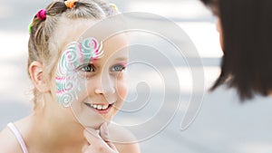 Cute little girl showing her beautiful face painting to mom