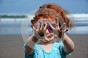 Cute little girl showing sandy hands on the Bali beach