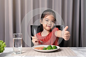 Cute little girl showing thumb showing eating healthy vegetables