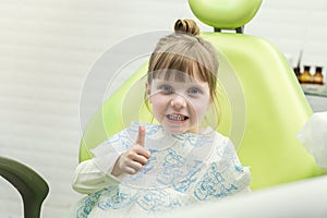 Cute little girl showing thumb up sign at dentist`s office clin