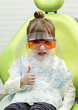 Cute little girl showing thumb up sign at dentist`s office clin