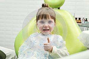 Cute little girl showing thumb up sign at dentist`s office clin