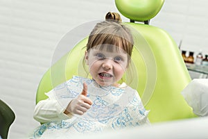 Cute little girl showing thumb up sign at dentist`s office clin