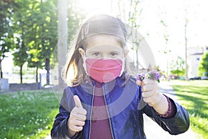 Cute little girl shows thumb up, wearing protective mask and holding bunch of wildflowers - Coronavirus time, Everything Will be