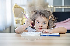 Cute little girl sit at desk at home doing homework, reading, writing and painting. Children paint. Kids draw.