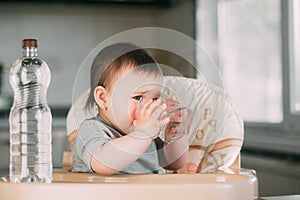 Cute little girl sitting in baby chair and drinking water