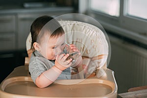 Cute little girl sitting in baby chair and drinking water