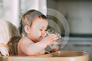 Cute little girl sitting in baby chair and drinking water