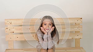 Cute little girl sitting on a bench in fashion Studio and posing for the camera