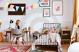 Cute little girl sitting at desk in her stylish vintage bedroom with workspace