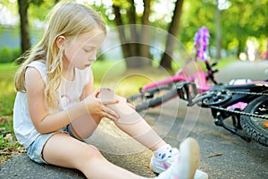 Cute little girl sitting on the ground after falling off her bike at summer park. Child getting hurt while riding a bicycle