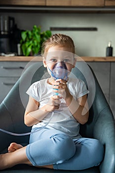 Cute little girl are sitting and holding a nebulizer mask leaning against the face at home on sick leave, airway