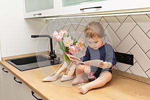 A cute little girl is sitting in the kitchen with a bouquet of pink tulips , beautiful gift postcard