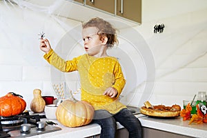 Cute little girl sitting on kitchen table and holding halloween dacorations spider