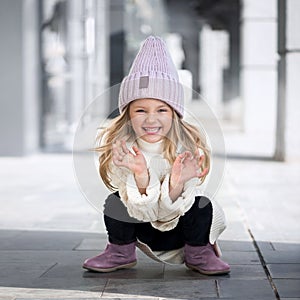 Cute little girl sitting and laughs in knitted hat