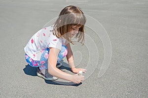 A cute little girl, sitting outside and drawing with chalk on the asphalt