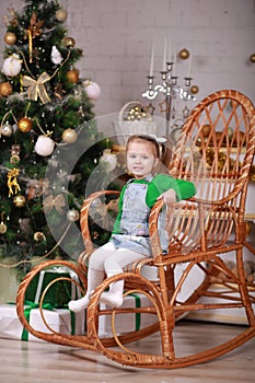 Cute little girl sitting in rocking chair near christmas tree