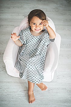 Cute little girl sitting on small armchair and smiling at camera