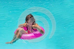 Cute little girl sitting on swimming ring donut in the swimming pool