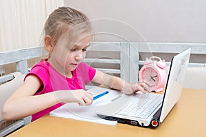 A cute little girl is sitting at a table and typing homework on a laptop to send to the teacher for review