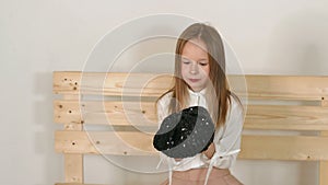 A cute little girl is sitting on a wooden bench on a white background in studio