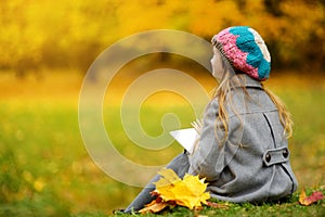 Cute little girl sketching outside on beautiful autumn day. Happy child playing in autumn park. Kid drawing with colourful pencils