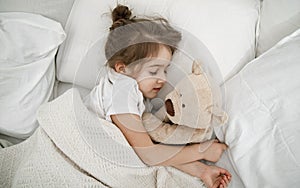 A cute little girl is sleeping in a bed with a Teddy bear toy