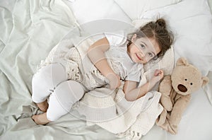 A cute little girl is sleeping in a bed with a Teddy bear toy