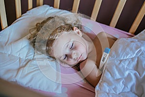 Cute little girl sleeping on a pillow in her bed with the thermometer.Measure the temperature. Girl is sick, the child has a cold