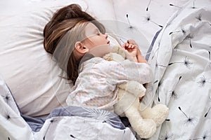 Cute little girl sleeping with teddy bear in bed