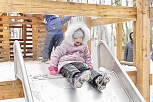 Cute little girl slide down the slide on a winter walk