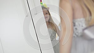 Cute little girl in a smart dress admires herself in the mirror