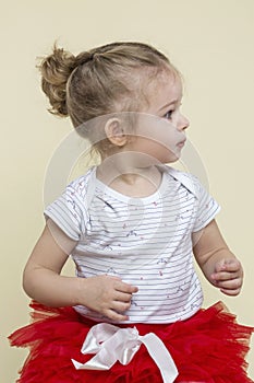 A cute little girl in a smart red skirt looks away. Happy childhood. Yellow background. Vertical