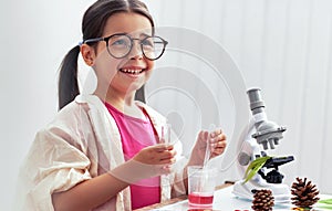 Cute little girl smiling and working with microscope and exploring plants. The kid in lab coat learning science in the school
