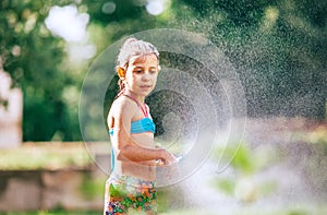 Cute little girl sprinkls a water for herself from the hose, makes a rain. pleasure for hot summer days. Happy careless childhood