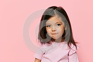 a cute little girl is standing on a pink background in a pink T-shirt, smiling happily and turning her head in