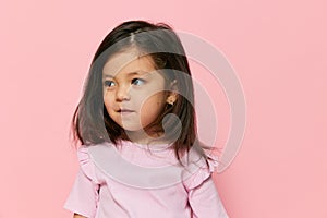a cute little girl is standing on a pink background in a pink T-shirt, smiling happily and turning her head in