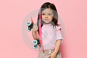 a cute little girl is standing on a pink background in a pink T-shirt, holding her skate in her hands, looking at it