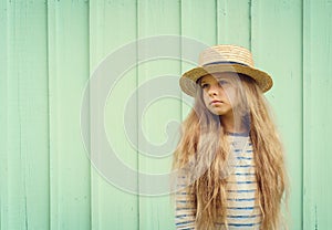 Cute little girl stands near a turquoise wall in boater hat and pensively looks aside. Space for text photo
