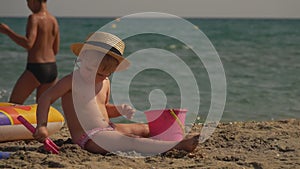 Cute little girl in a straw hat builds a sandcastle on the beach