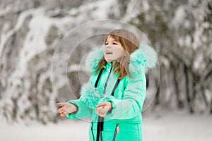 Cute little girl stretches her hand to catch falling snowflakes.