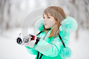 Cute little girl stretches her hand to catch falling snowflakes.