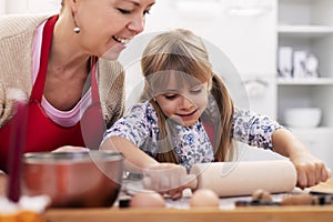 Cute little girl stretching the cookie dough at the kitchen table with her mother