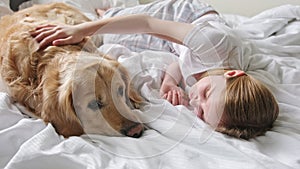 Cute Little Girl Stroking Adorable Golden Retriever Dog, Lying With Lovely Pet In Bed